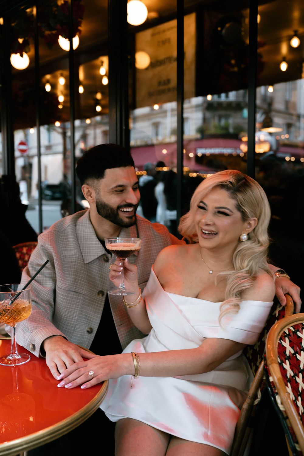 A couple shares drinks and laughter at a cozy outdoor cafe with warm lighting and romantic ambiance.