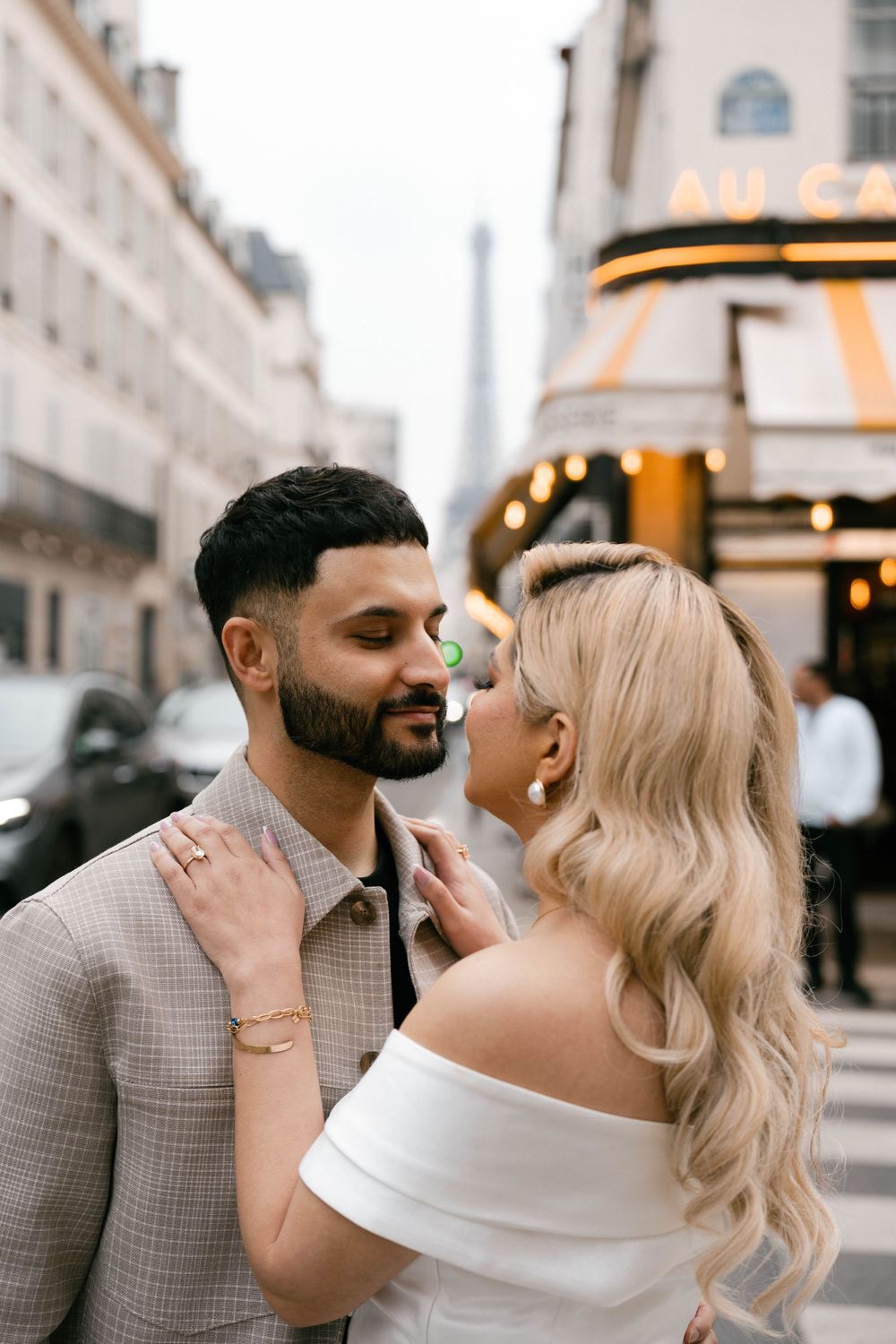 A romantic couple embraces on a Parisian street with the Eiffel Tower visible in the background.