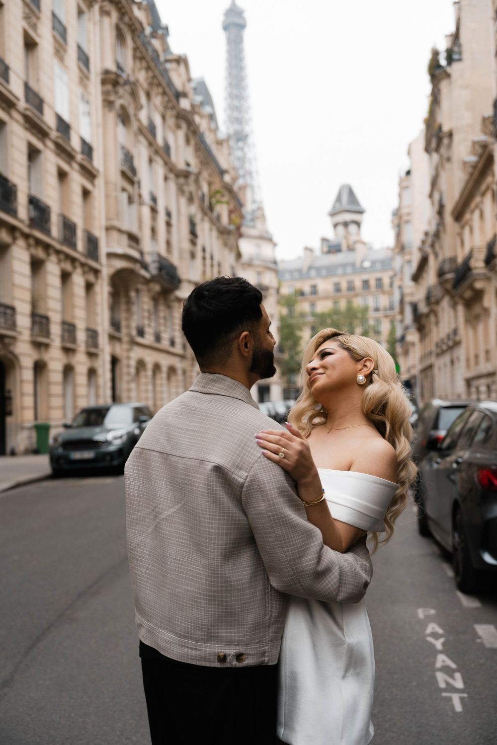 Romantic couple embraces on a charming Parisian street with the iconic Eiffel Tower visible in the background.