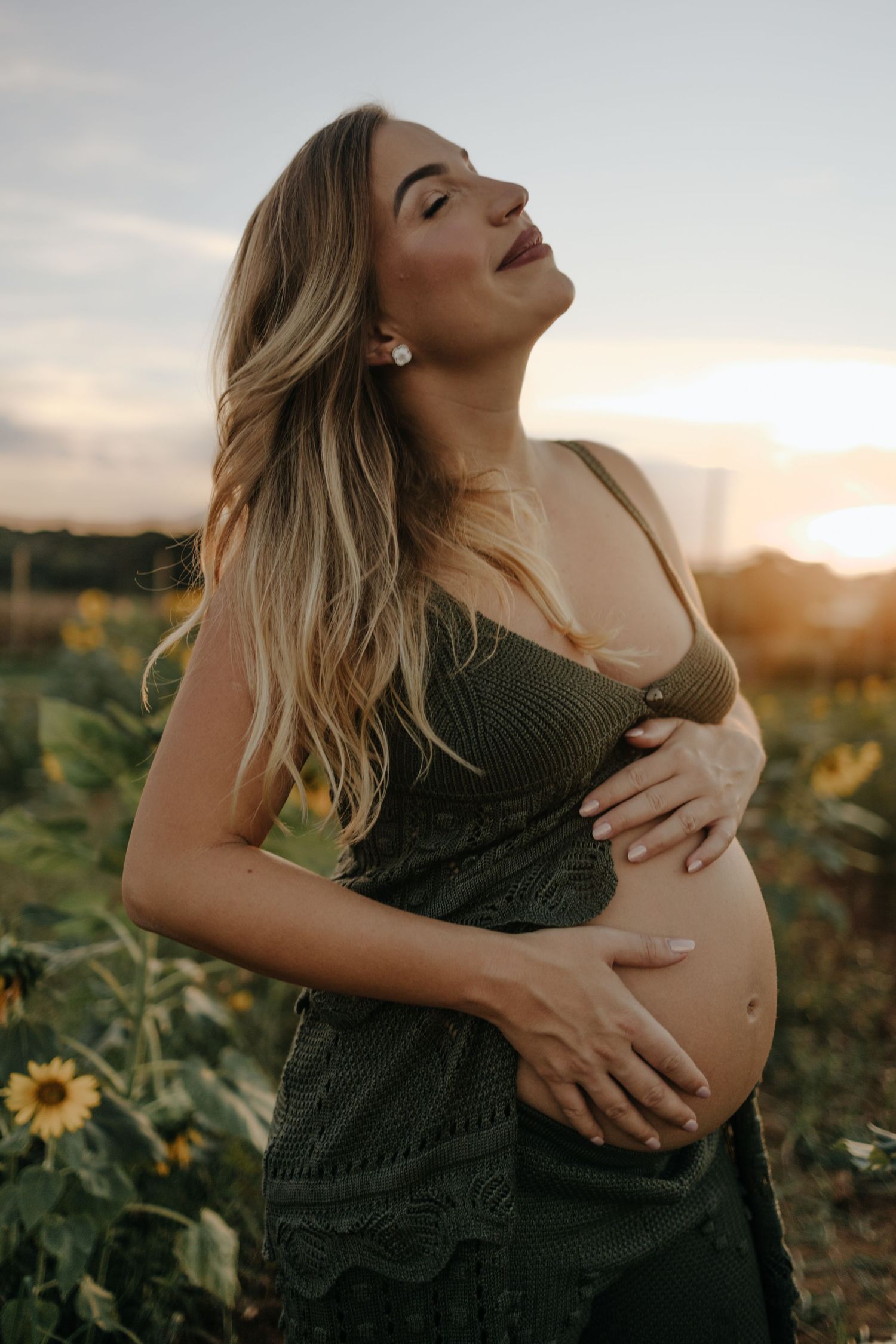 Pregnant woman holding her belly in a field of sunflowers, during sunset