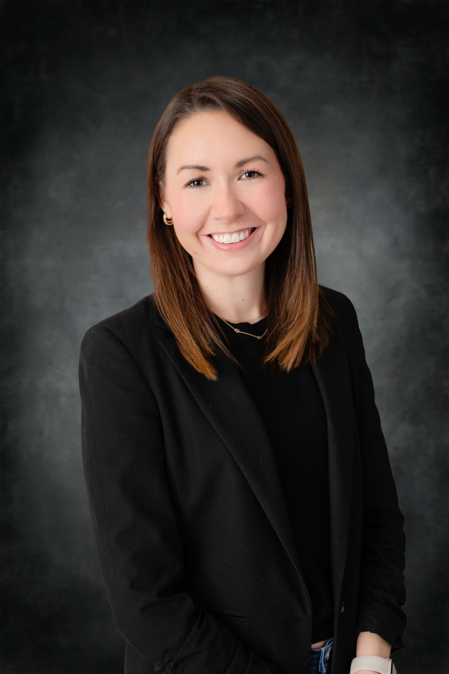 Professional studio portrait of a smiling professional in a black blazer against a dark gray background.