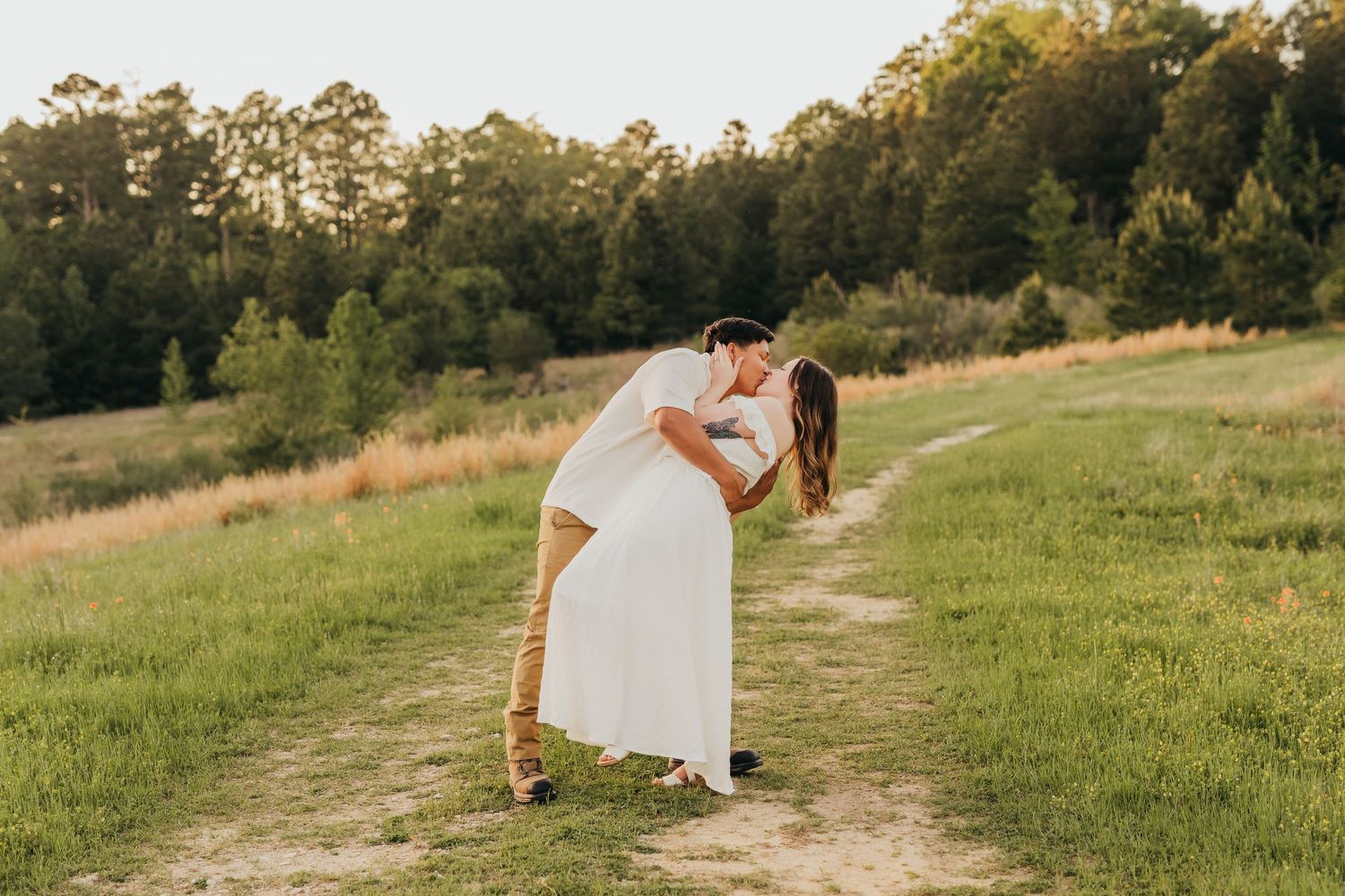 A couple embraces in a tender moment on a grassy hillside path during golden hour at sunset in Tyler, Tx.