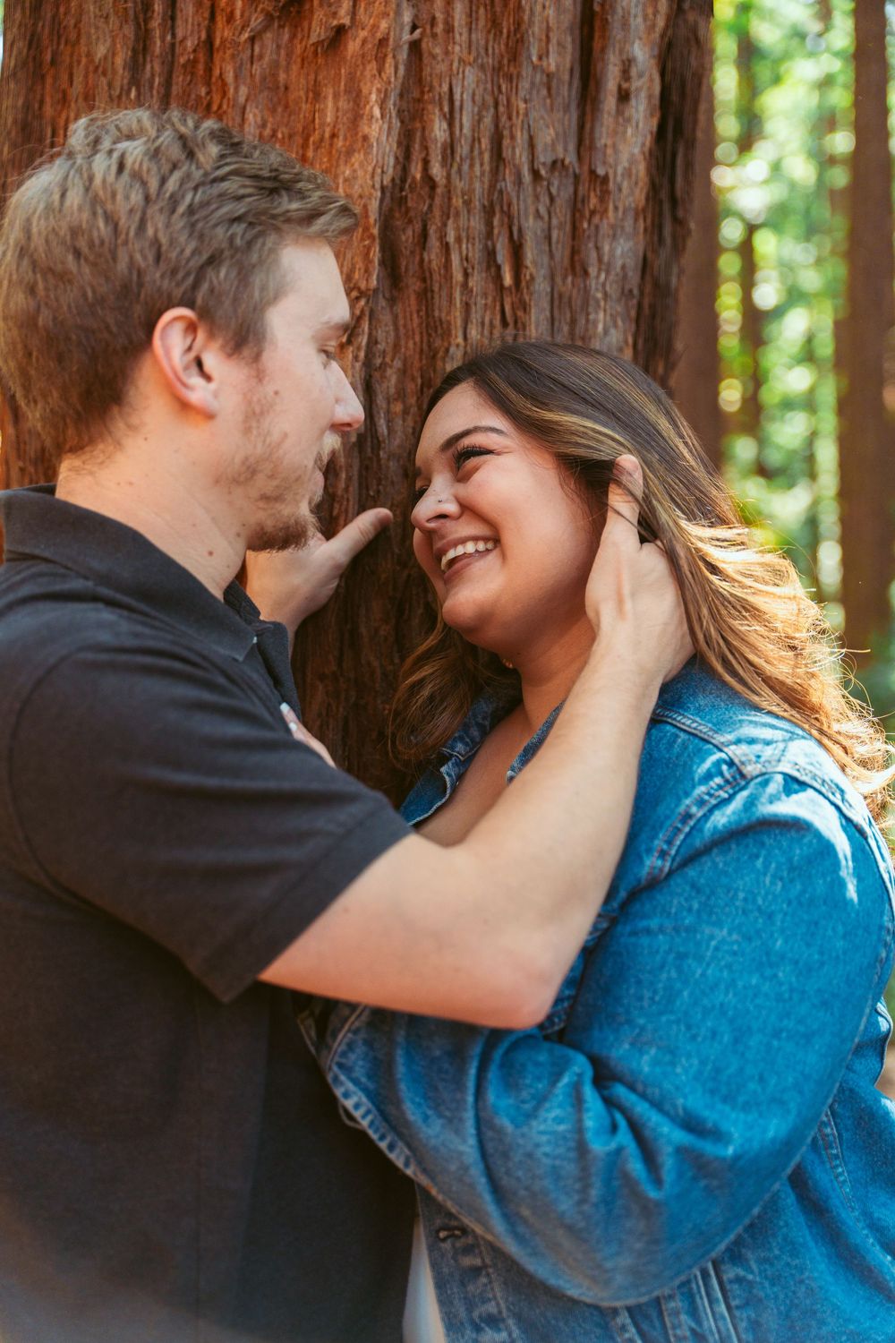 A couple shares an intimate moment among towering redwood trees.