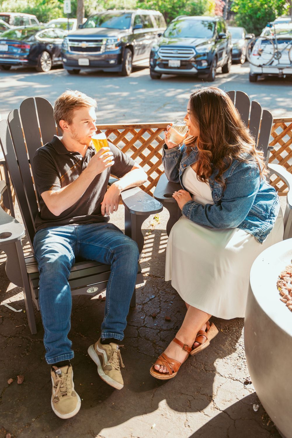 A couple sitting in Adirondack chairs sharing drinks and conversation outdoors.