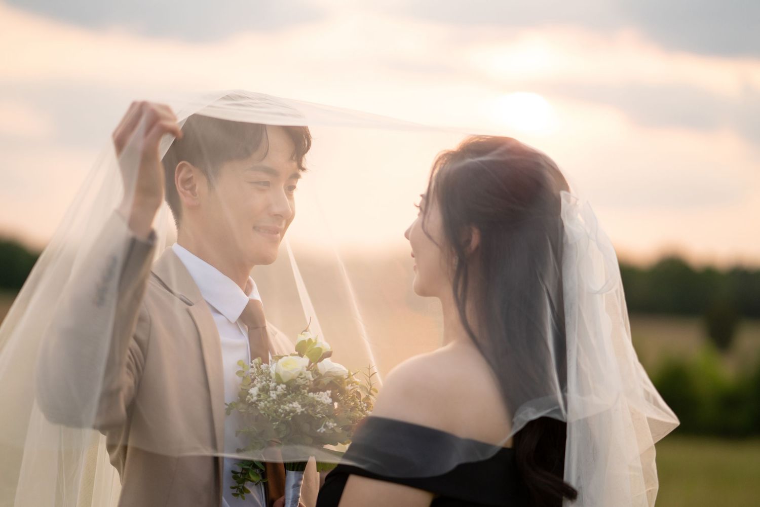 Romantic sunset portrait of a couple in wedding attire holding a bouquet of white flowers.