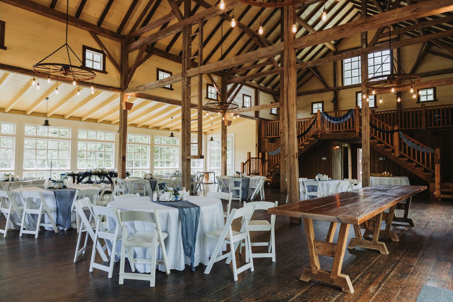 Rustic interior of a banquet hall with exposed wooden beams, white chairs, and natural lighting through windows.