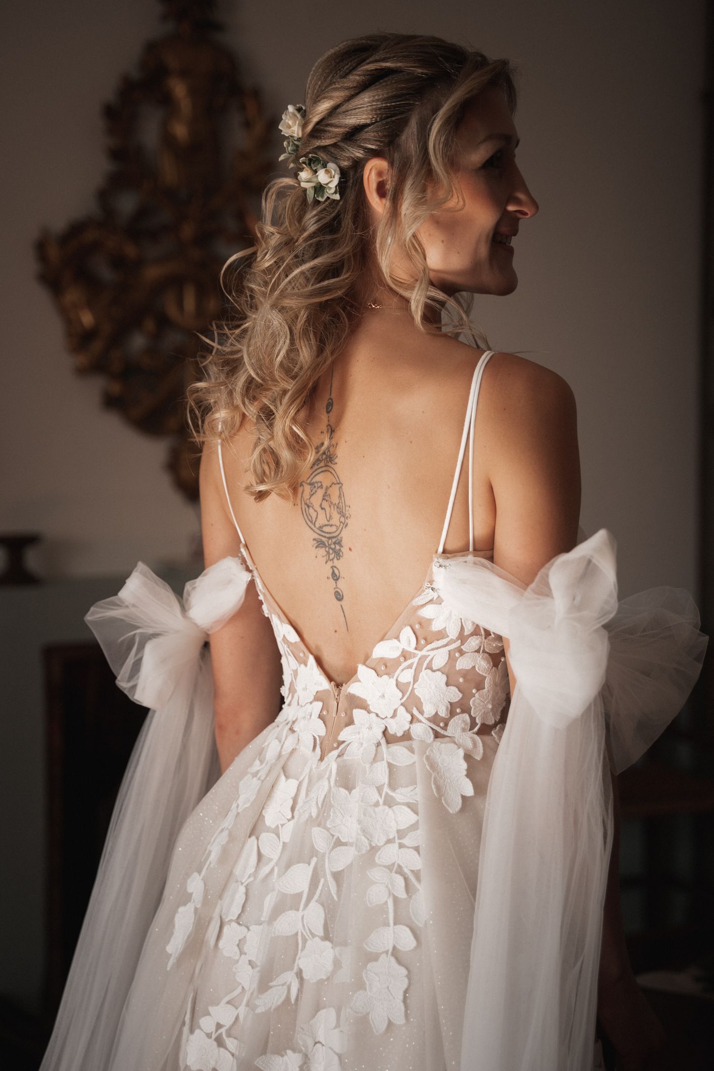 Elegant backless wedding dress with floral appliques and flowing tulle details shown from behind in soft lighting.
