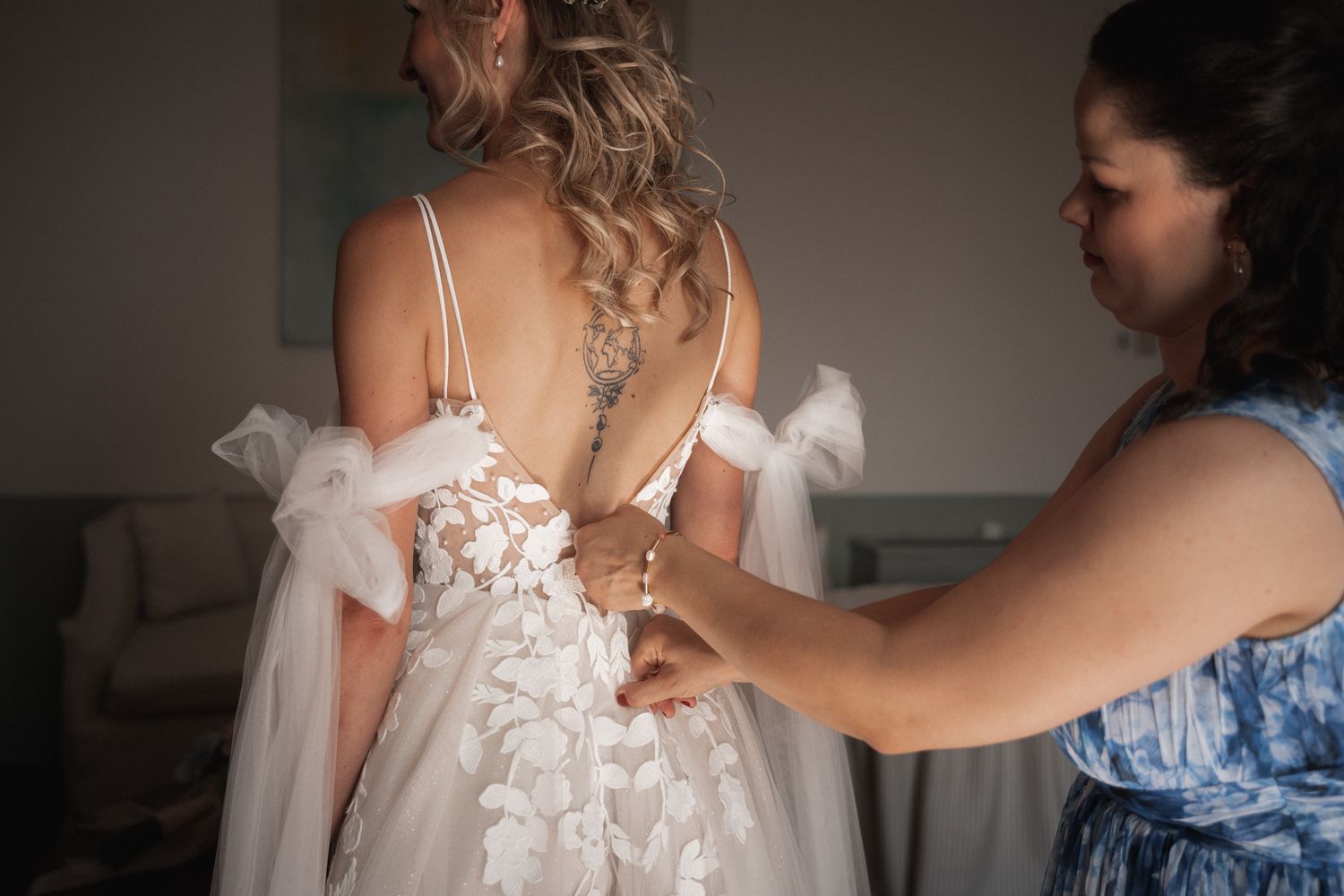 A helper adjusts the delicate floral lace details on a bride's wedding gown before the ceremony.