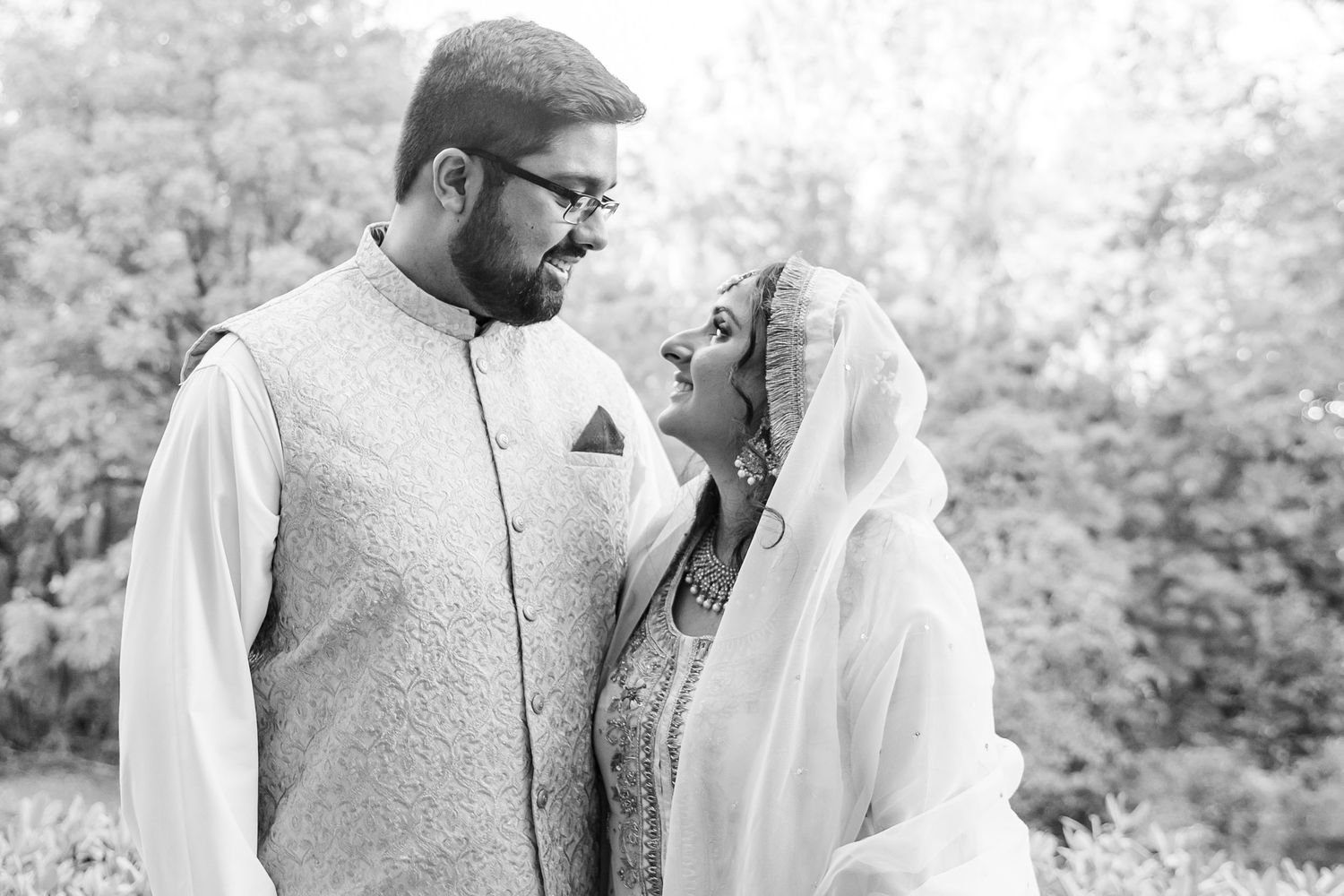 Couple in traditional South Asian wedding attire sharing tender moments in a garden setting.