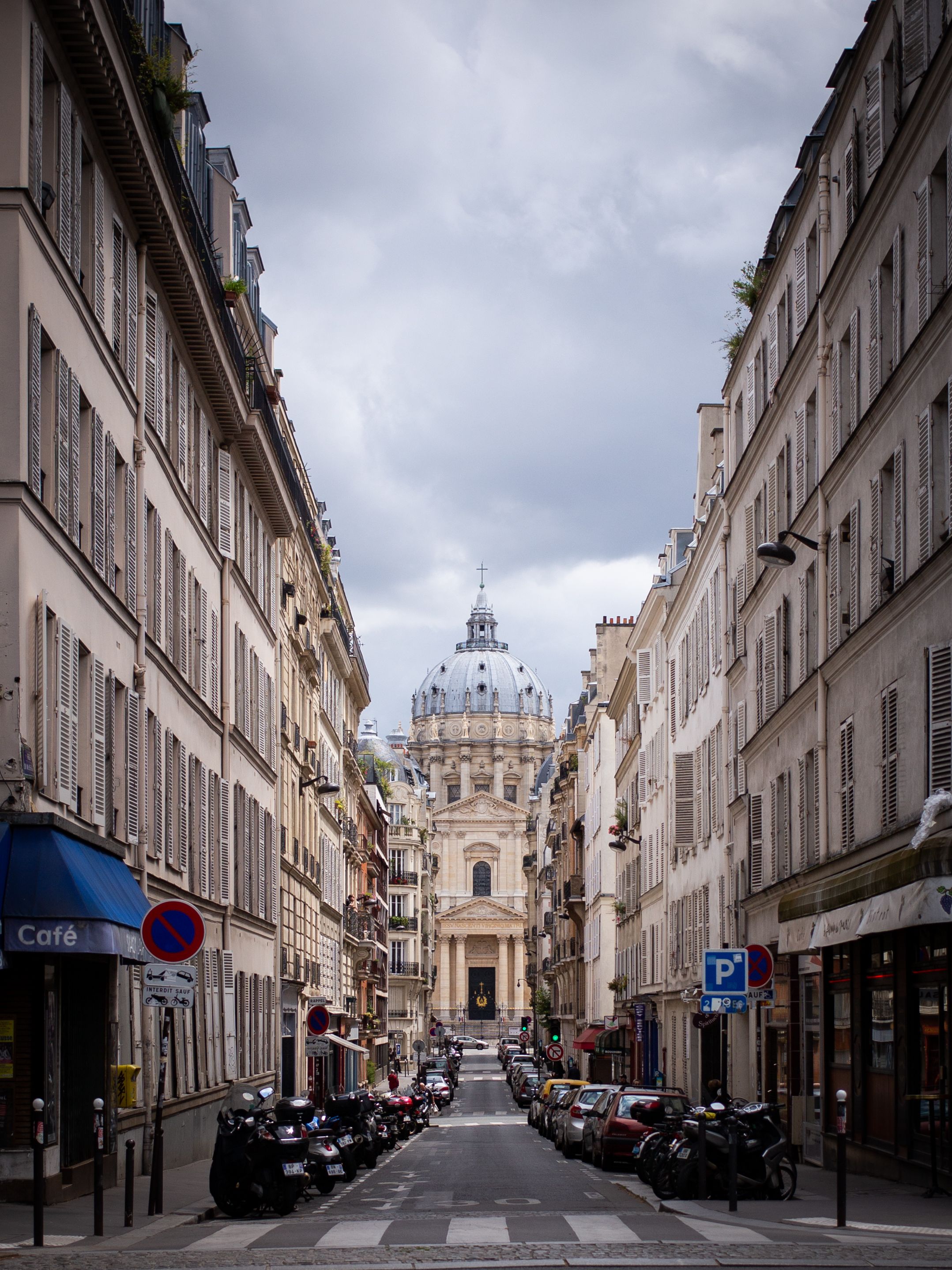 Narrow Parisian street lined with classic buildings leading to a domed church in the distance.