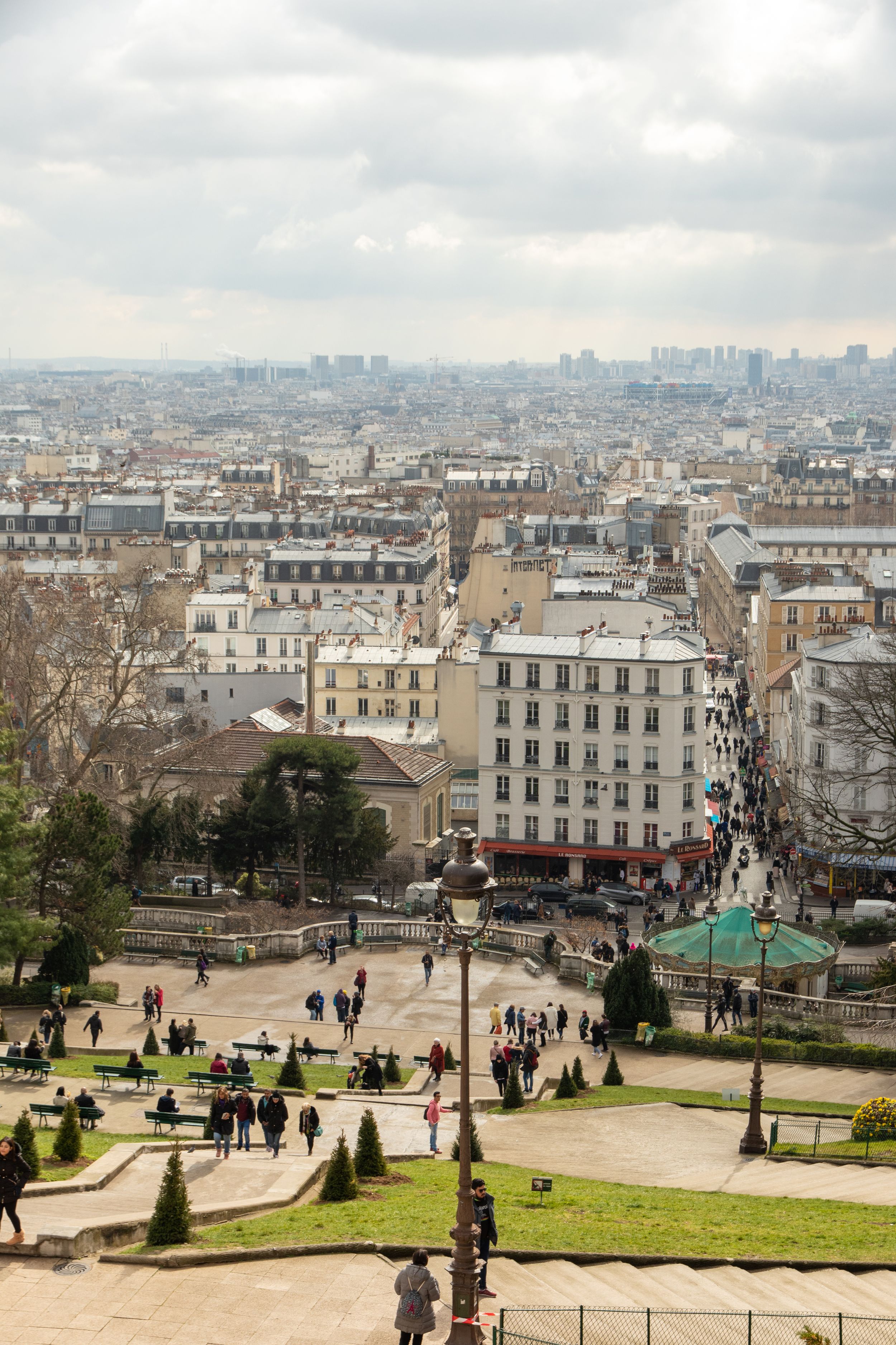 Aerial view of historic Parisian buildings and streets from Montmartre with city skyline in background.