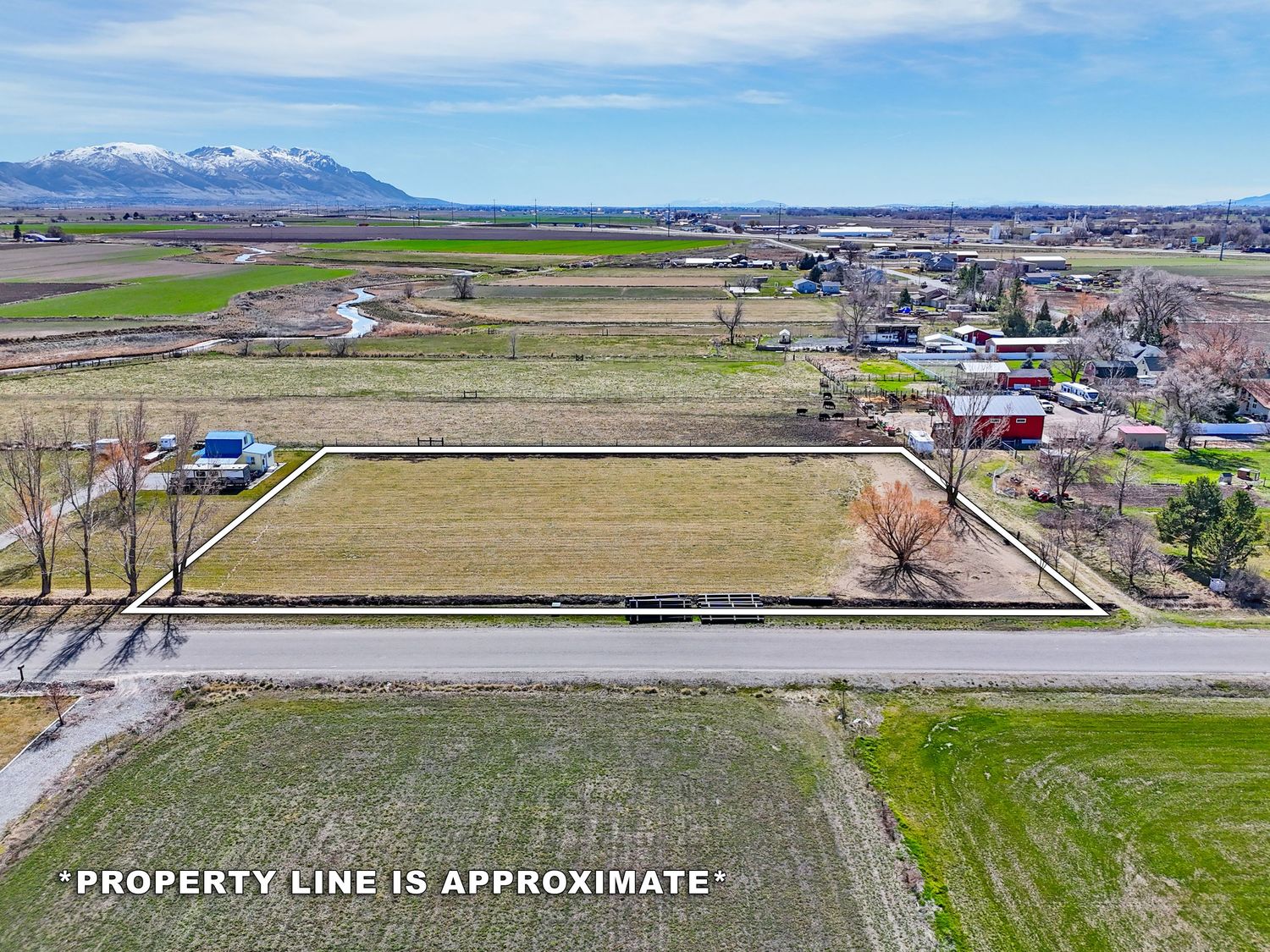 Aerial view of lush green farmland fields near a lake with mountains visible in the background. Captured by Slate Media (best in UT)
