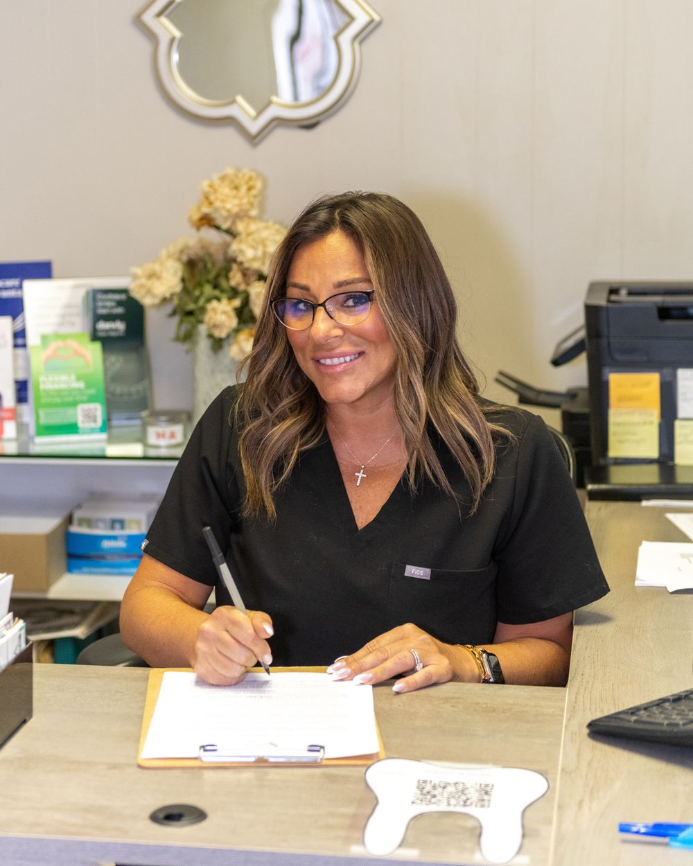 Medical professional completing paperwork at office desk with decorative mirror in background.