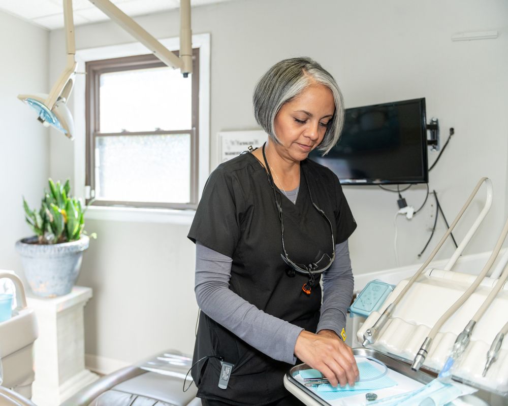 Healthcare worker in scrubs preparing dental equipment in modern office setting.