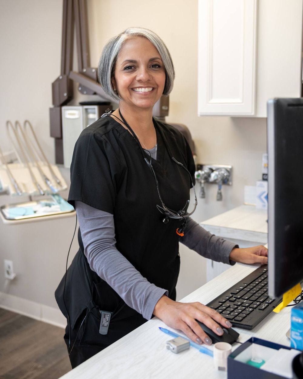 Medical professional in layered scrubs working at computer station in clinical setting.