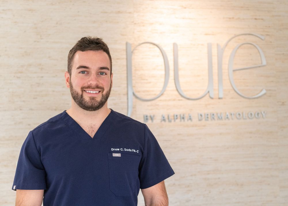 Medical professional in navy scrubs smiling in front of Pure branded wall.