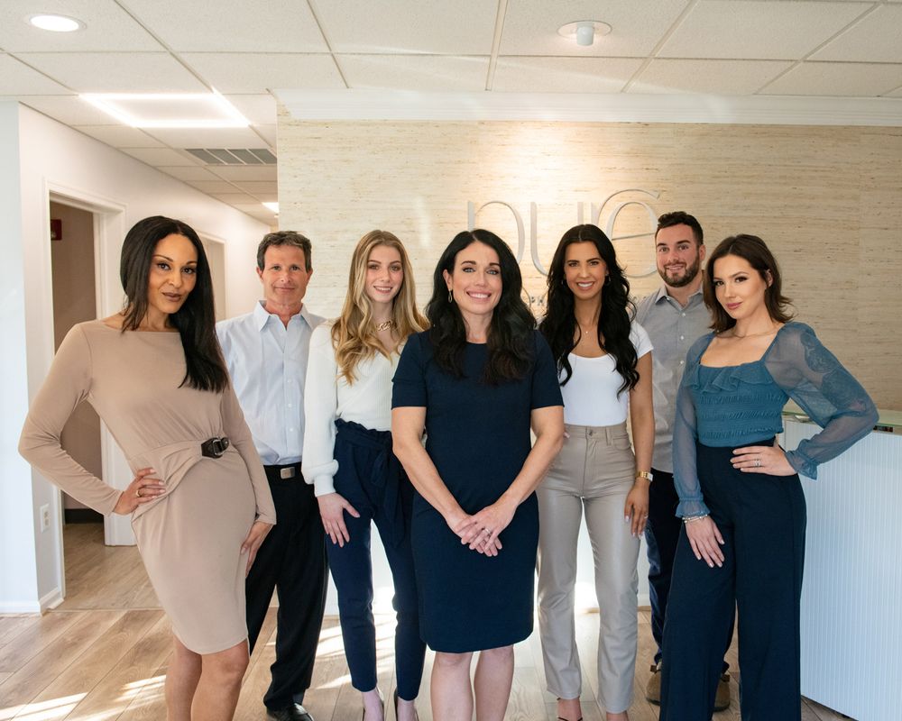 Professional team photo of staff members in business attire standing in modern office hallway.