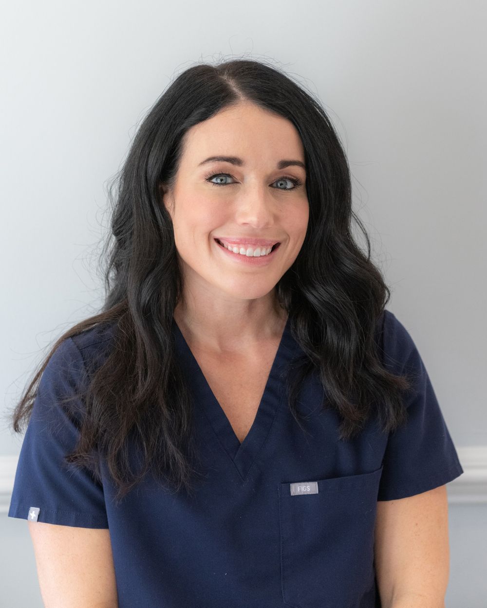 Healthcare professional in navy scrubs smiling in clinical setting.