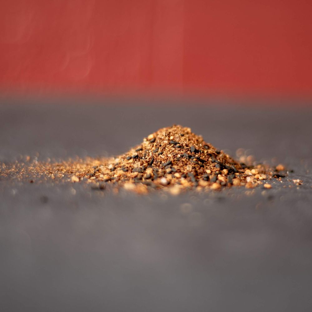 Close-up of golden brown spice powder piled on dark surface against red background.