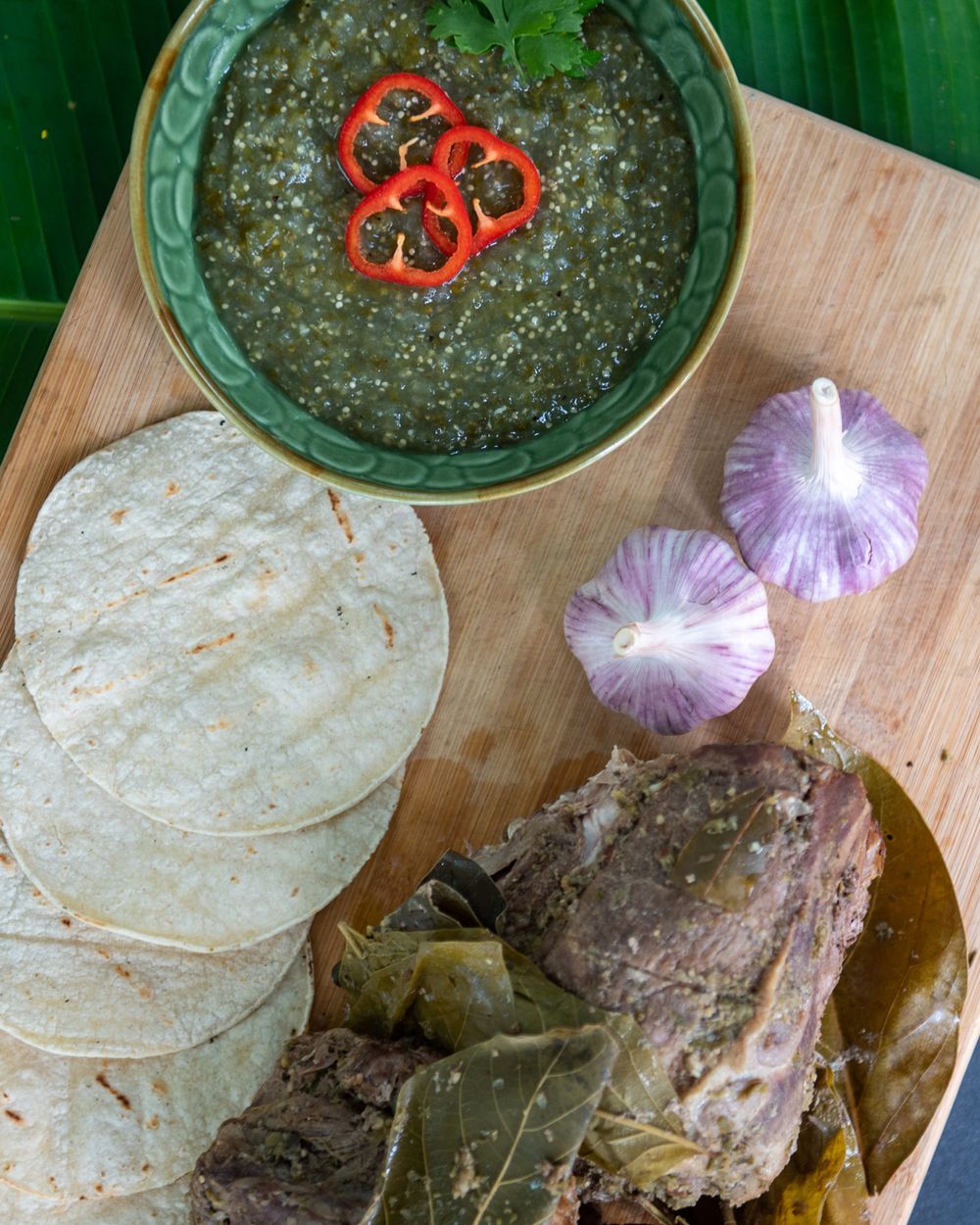 Mexican salsa verde with tortillas, cherry tomatoes and purple onions on a wooden board.