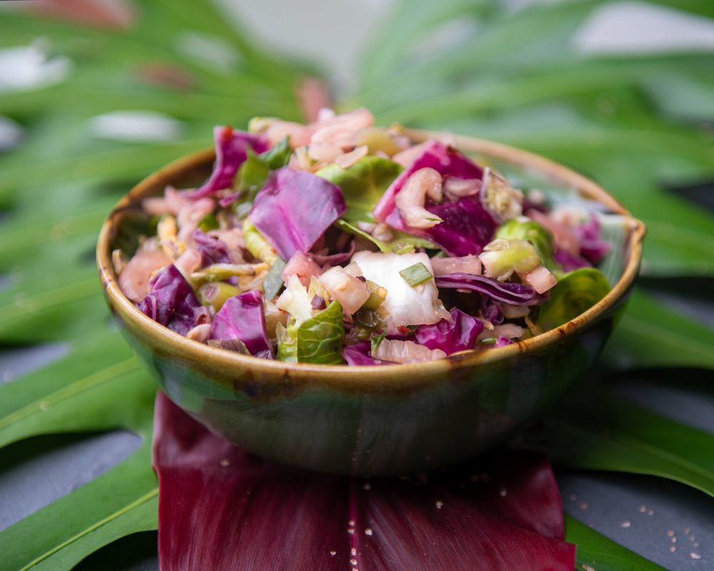 Vibrant Asian slaw with purple cabbage and herbs served in a ceramic bowl on tropical leaves.