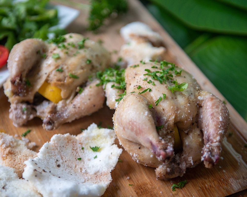 Seasoned quail birds garnished with fresh herbs on a wooden cutting board.