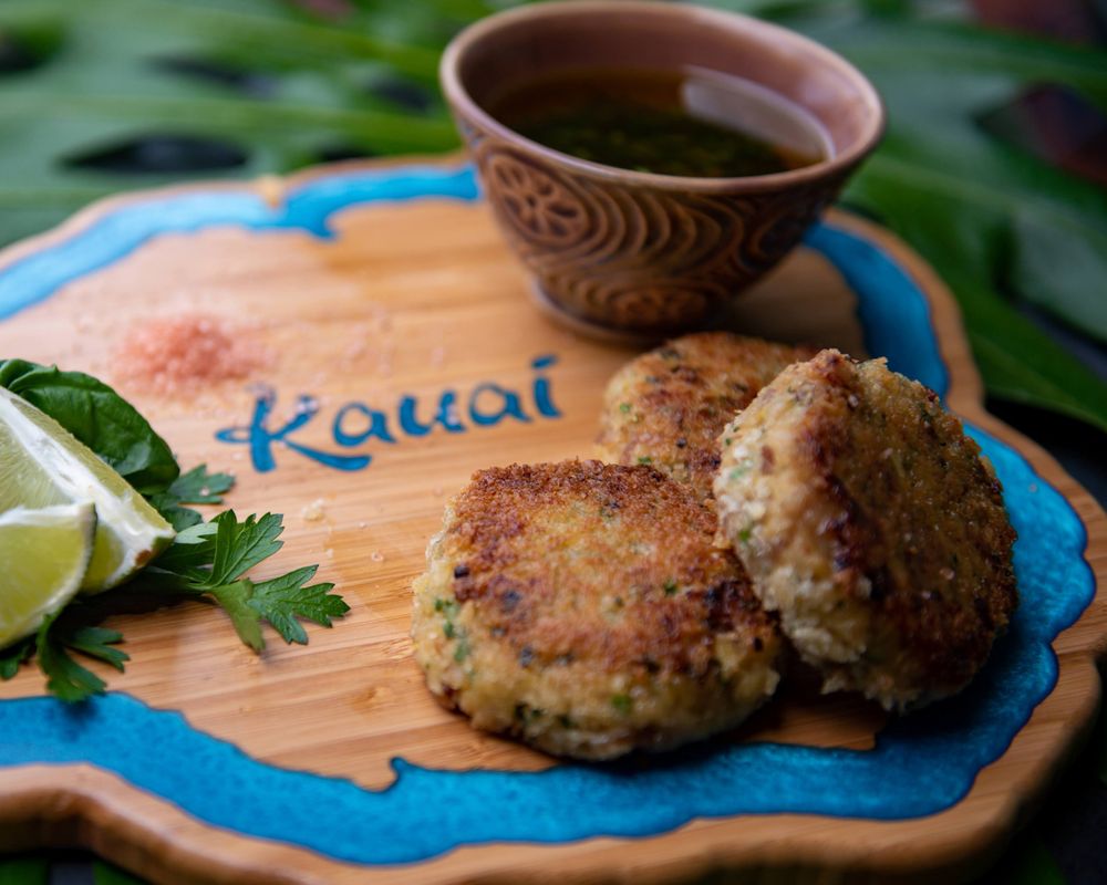 Homemade crab cakes served on a Kauai-themed wooden board with lime and hot tea.