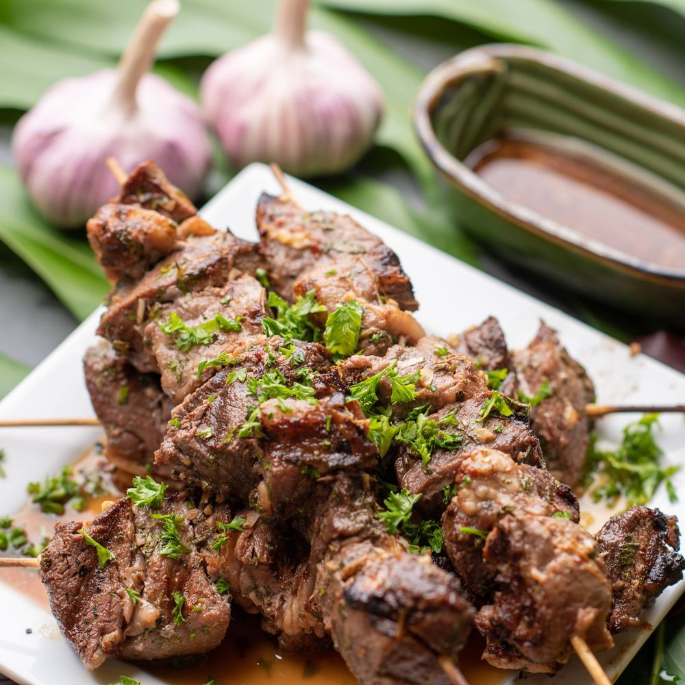 Grilled meat skewers garnished with fresh herbs and served with a dipping sauce.