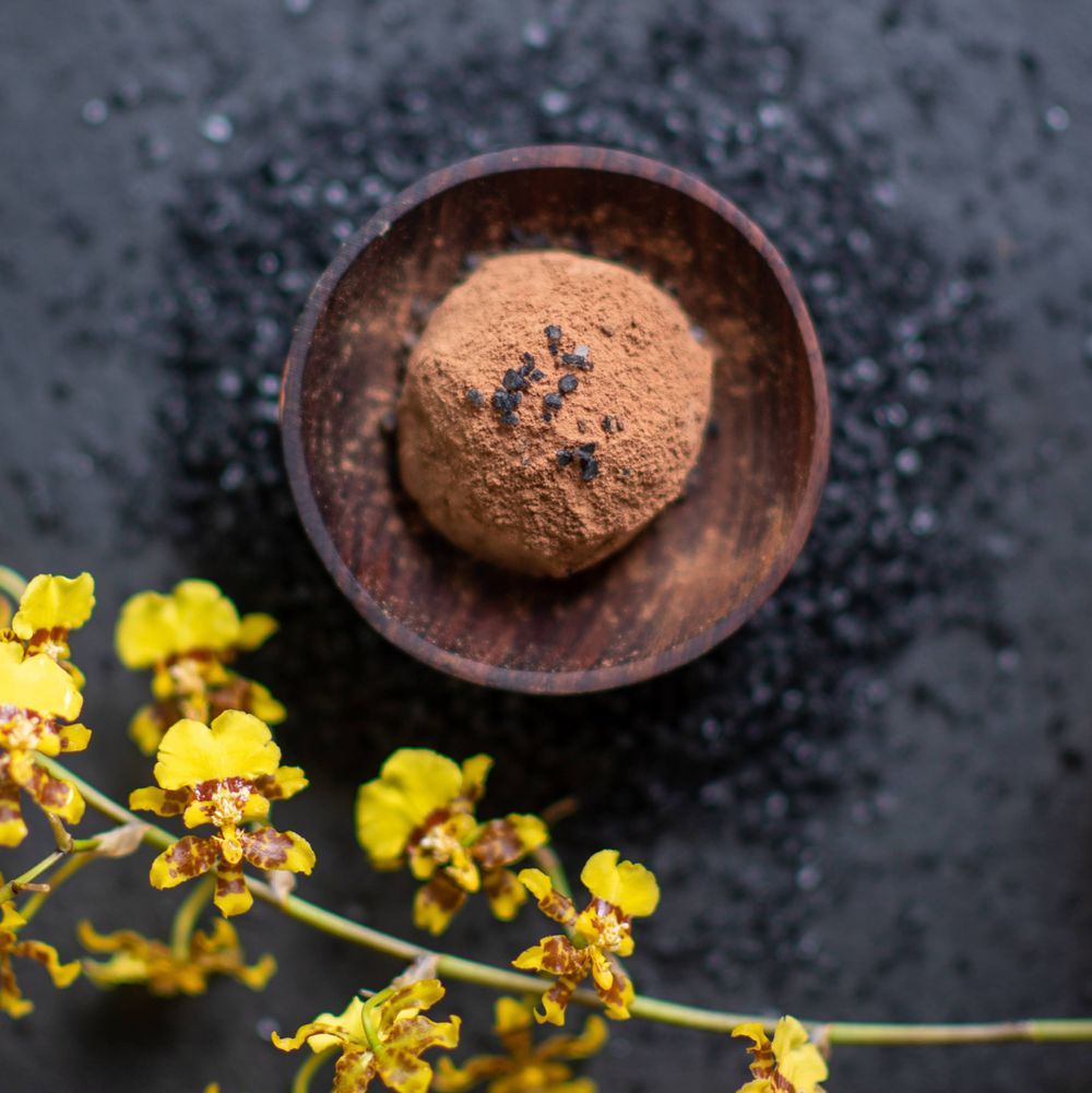 Dark cocoa powder in a wooden bowl with yellow flowers against a black textured background.