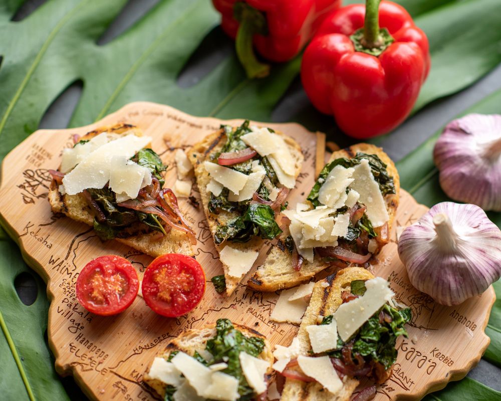Rustic bruschetta topped with shaved parmesan, tomatoes and herbs on a wooden board.