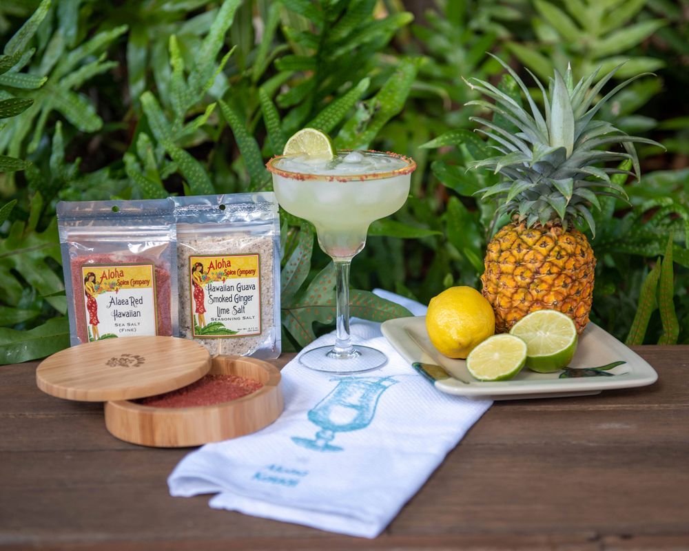 Tropical margarita setup with fresh pineapple, limes, and cocktail mixers on wooden table.