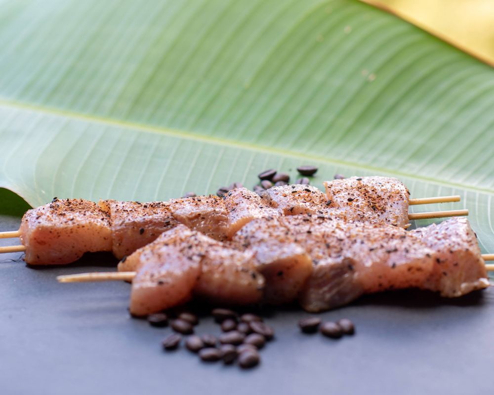 Grilled meat skewers on banana leaf with coffee beans and spice rub.