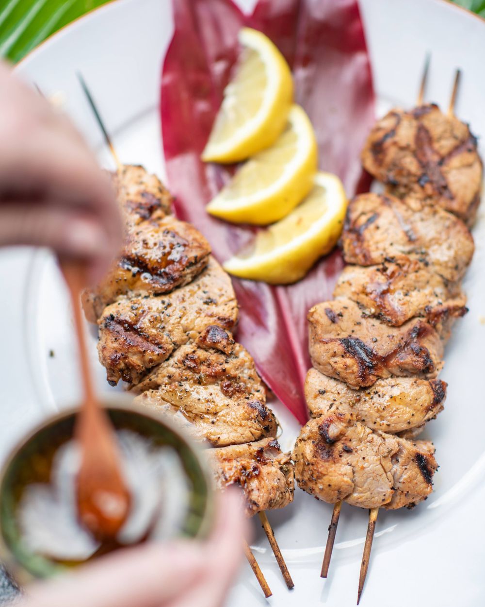 Grilled chicken skewers served with fresh lemon slices on a white plate.