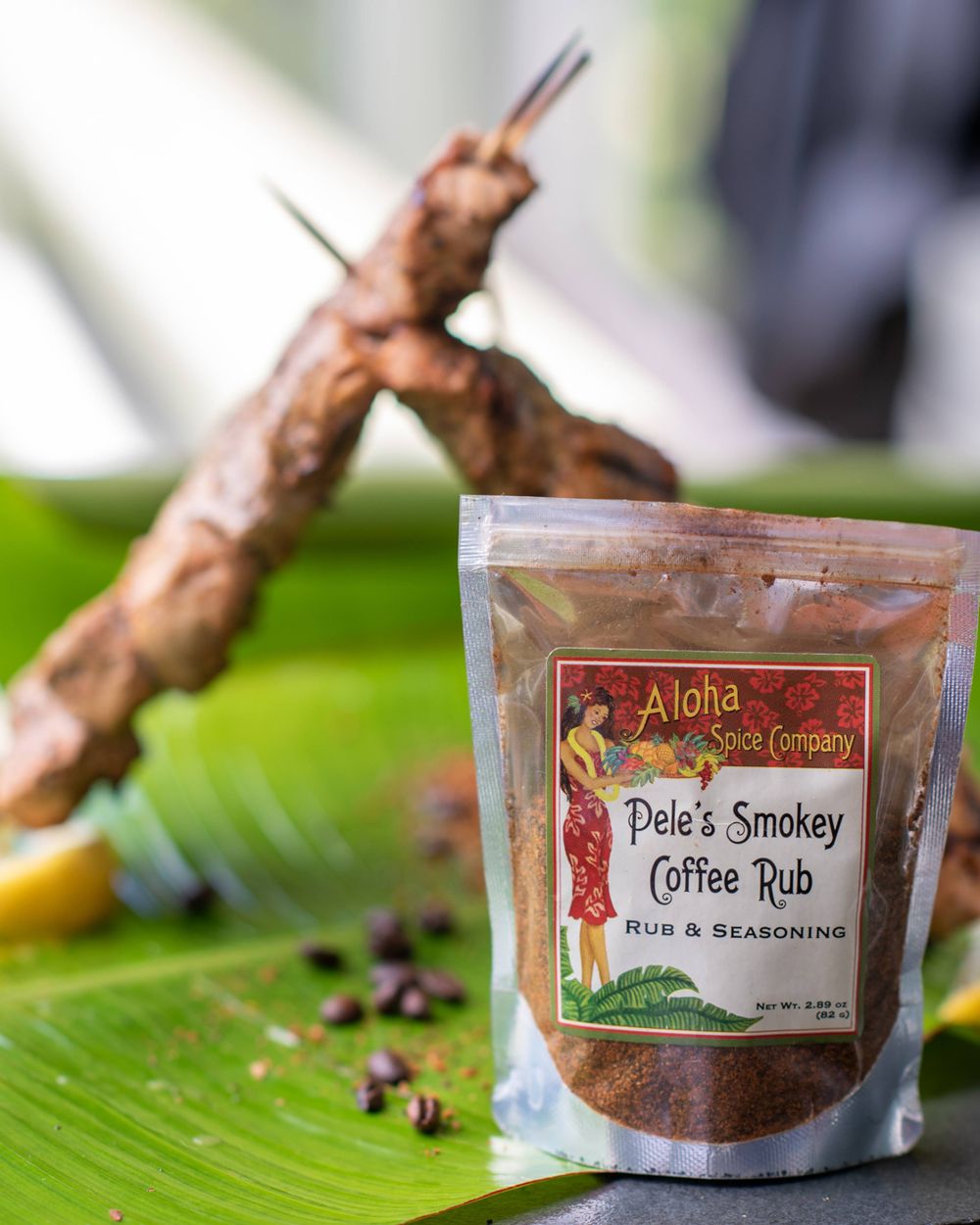 Grilled meat skewer with Alola coffee rub seasoning package on a banana leaf.