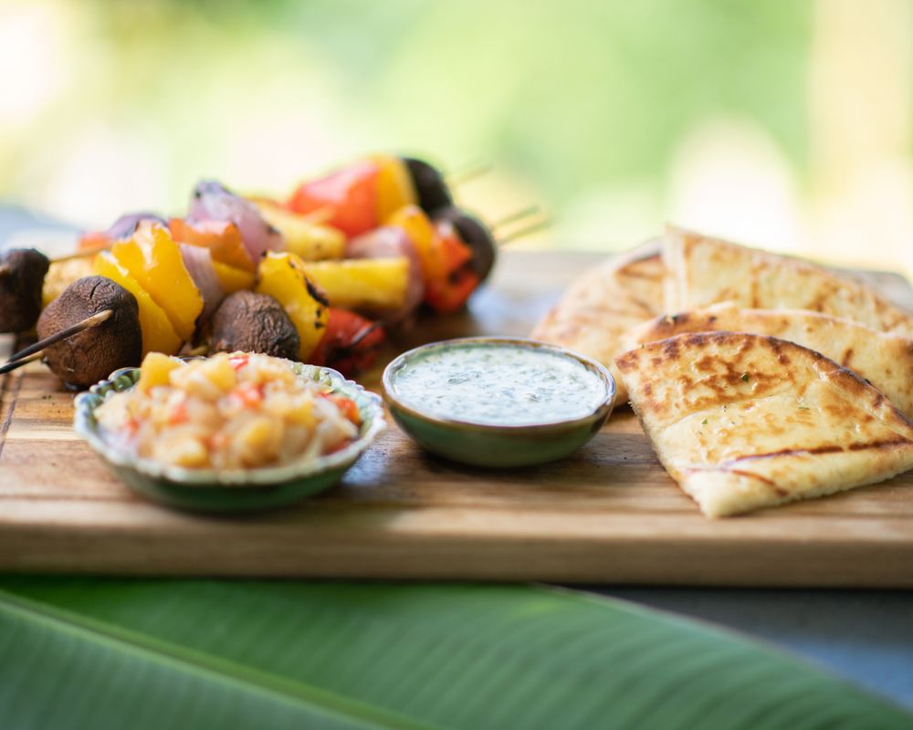 Wooden board with grilled vegetables, dipping sauces and flatbread served on a tropical leaf.
