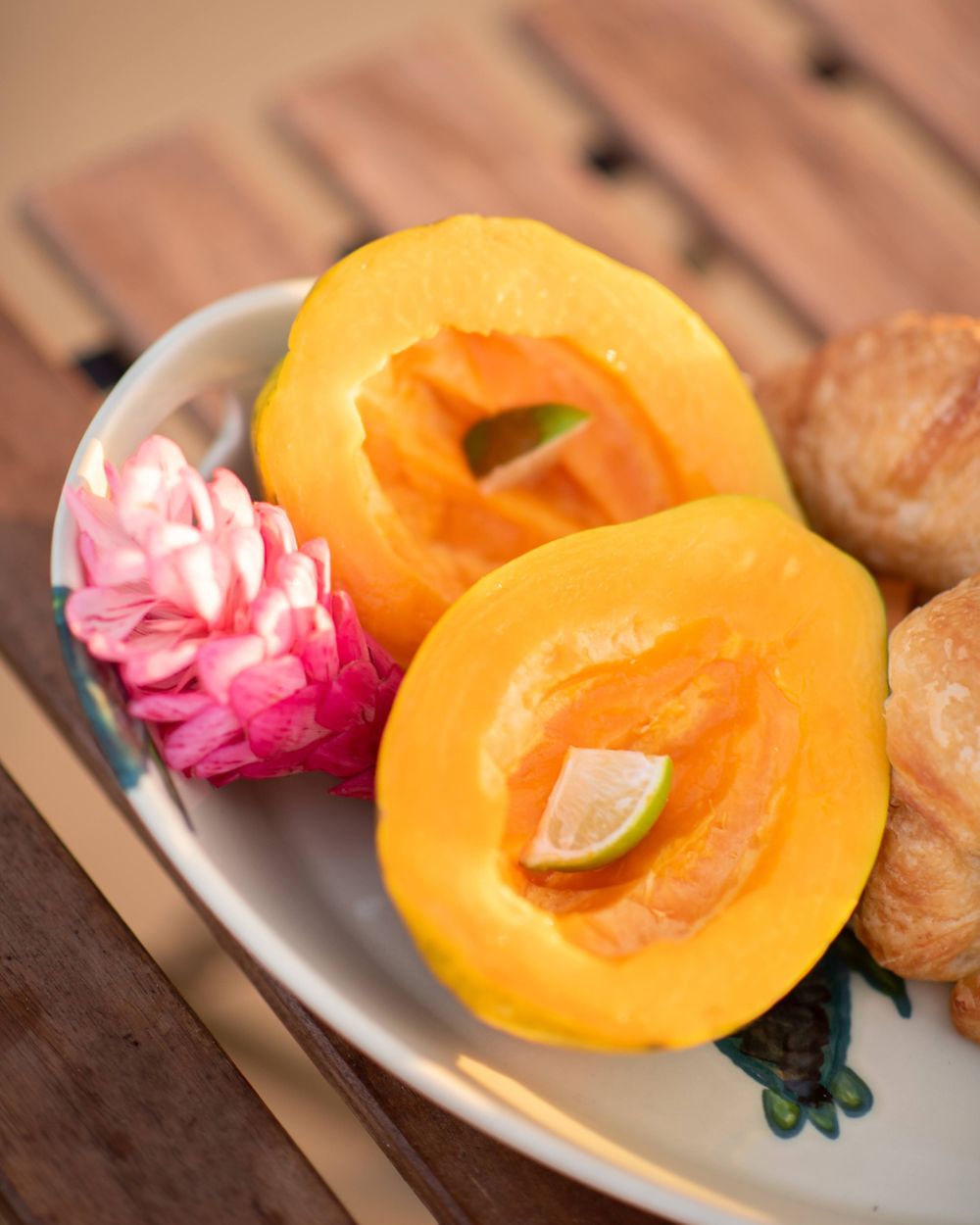 Fresh cut tropical loquats with pink flower garnish and pastries on decorative plate.