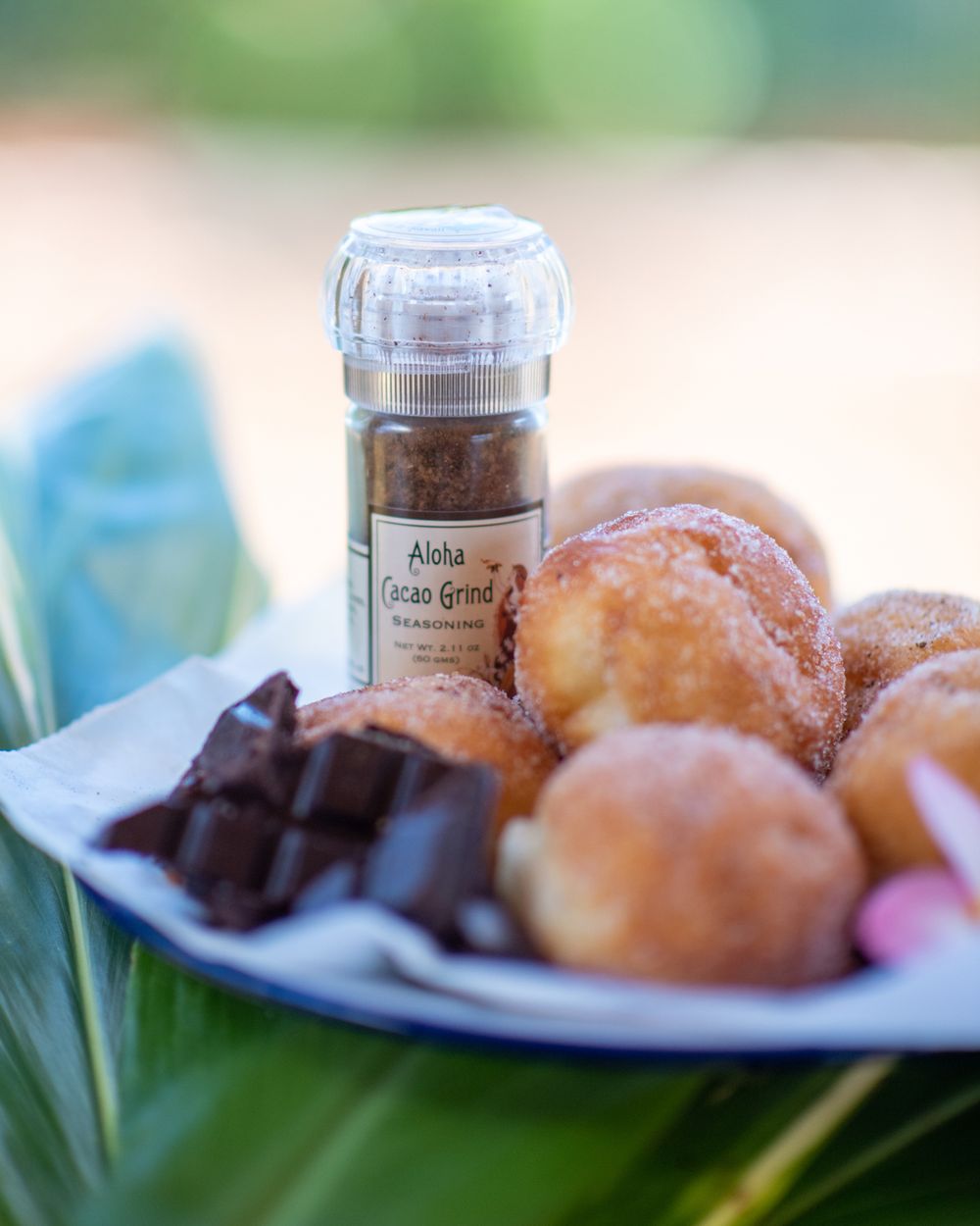 A plate of fresh donuts and chocolate pieces next to a spice jar on a blurred green background.