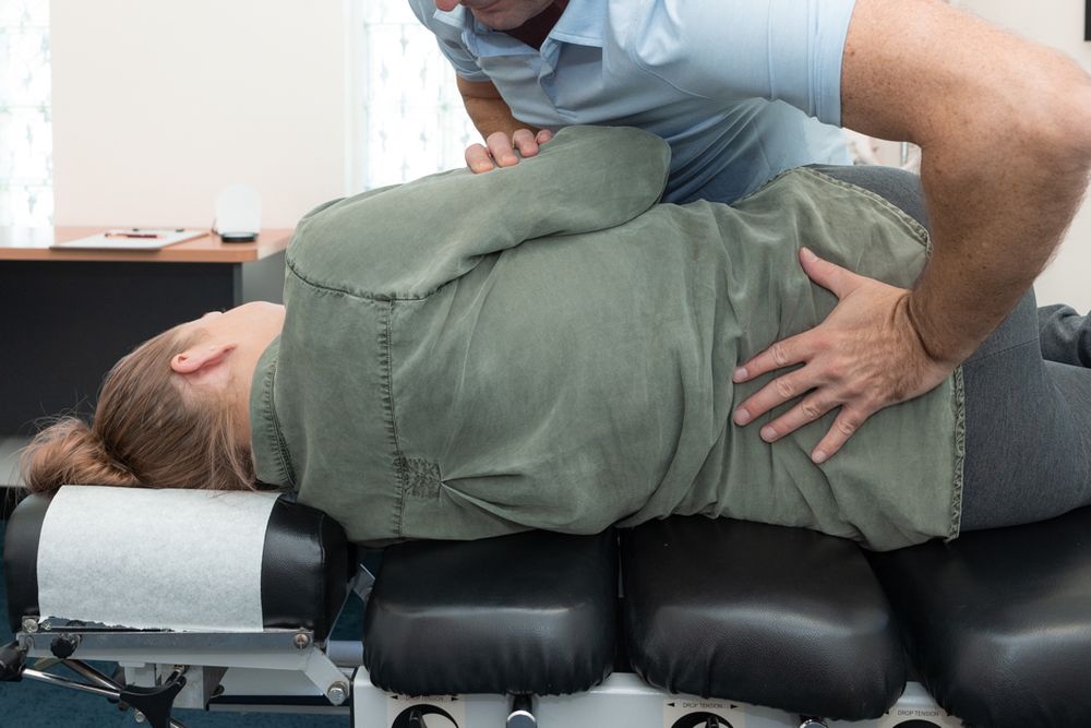 Chiropractor performs spinal adjustment treatment on patient lying on black adjustment table.