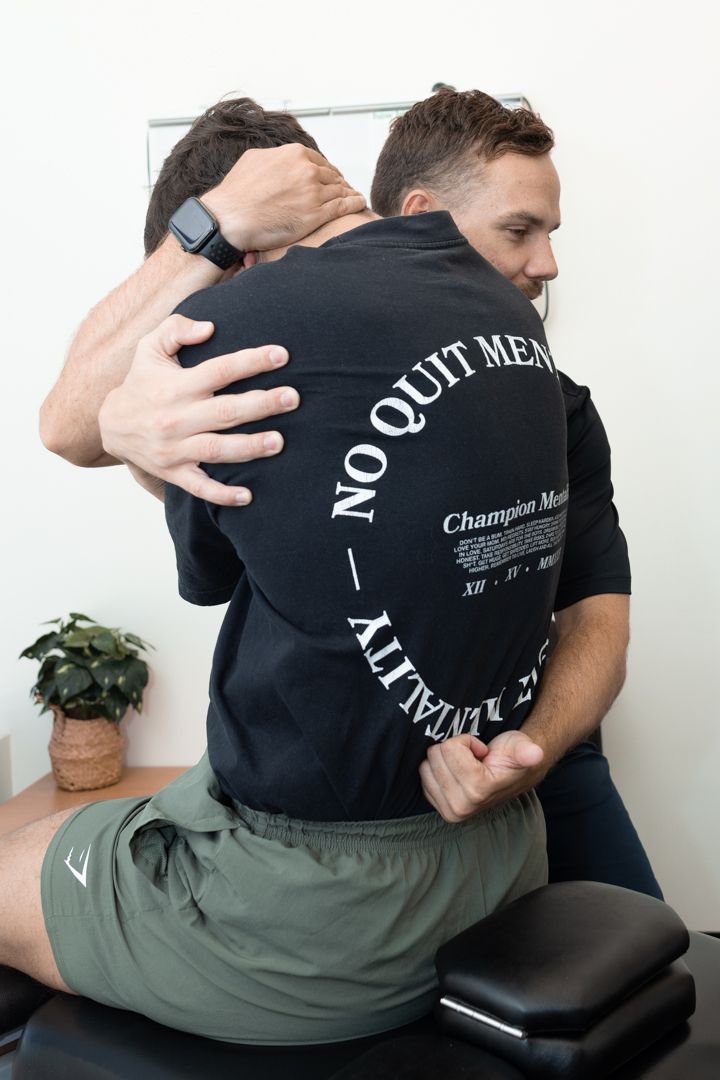 Chiropractor performs manual adjustment on patient wearing black t-shirt with text on treatment table.