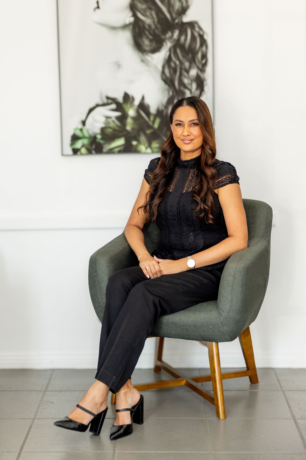 A woman in black attire sits elegantly in a modern grey accent chair.