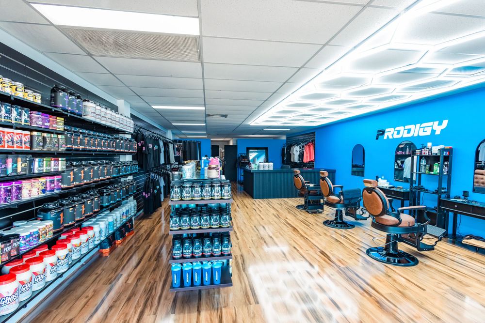 Modern barbershop interior with blue walls, wooden floors, and retail product displays along the wall.