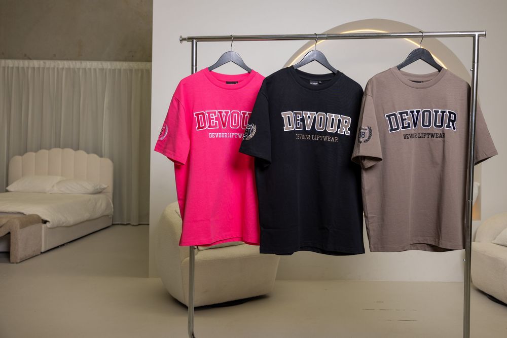 Collection of crop top t-shirts in pink, black, and beige displayed on hangers against a neutral wall background.