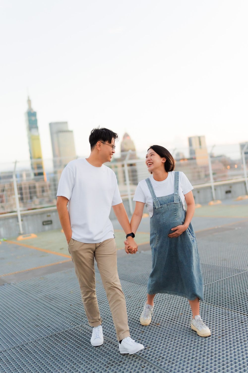 Couple sharing a joyful moment while walking on rooftop against city backdrop.