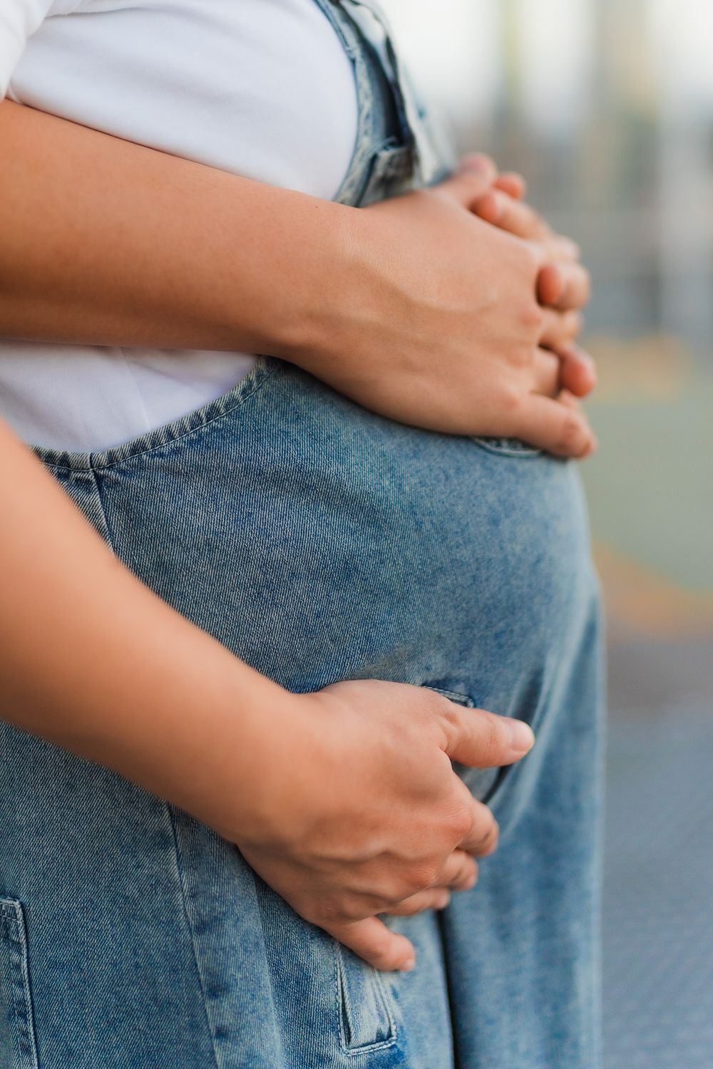 Close-up of hands forming heart shape over denim overalls against urban backdrop.