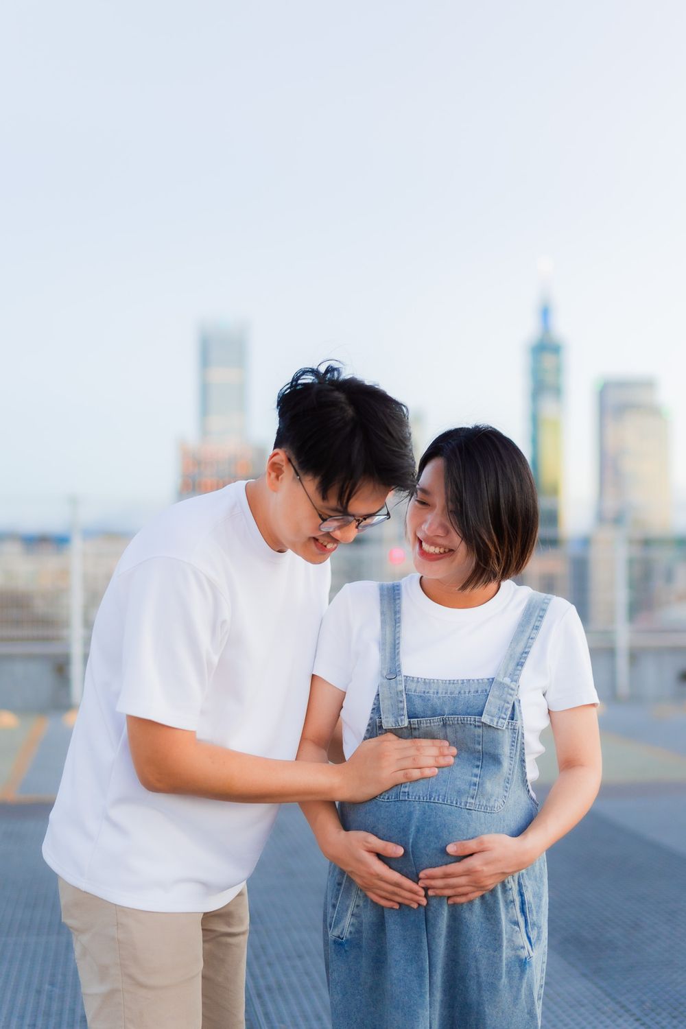 Tender moment between couple as they share loving gesture with baby bump on urban rooftop.