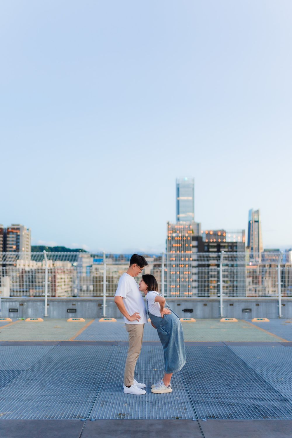 Romantic couple embraces on rooftop with dramatic city skyline in background during sunset.