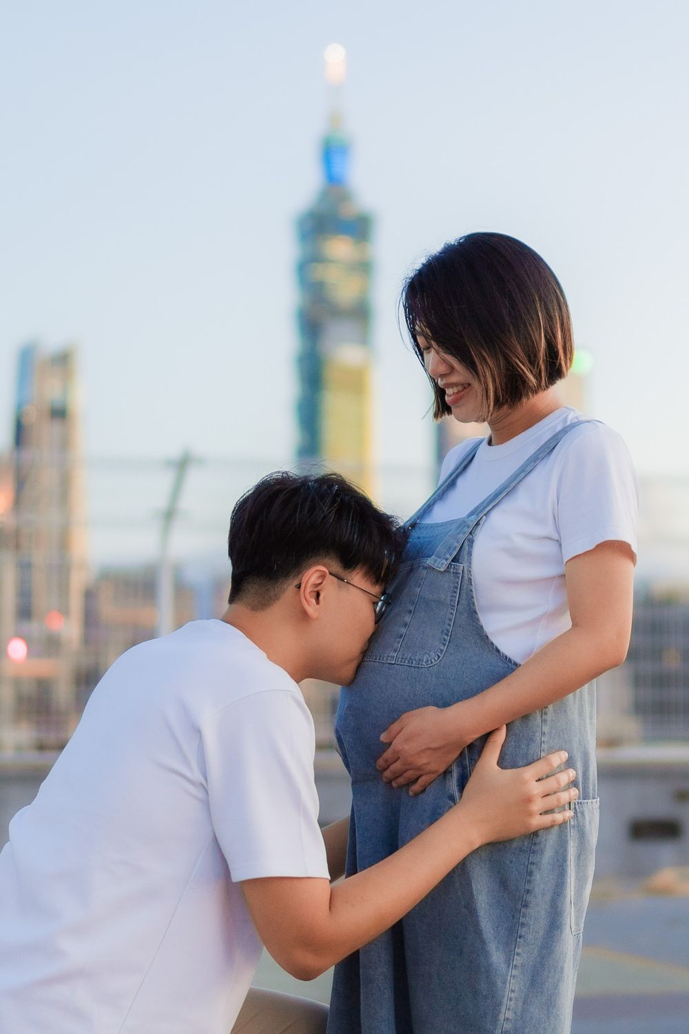 Intimate moment captured between couple during maternity photoshoot with Taipei 101 visible in background.