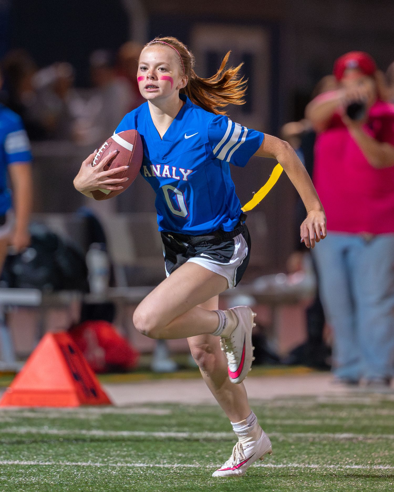 Athlete wearing blue jersey runs with football during competitive game on outdoor field.