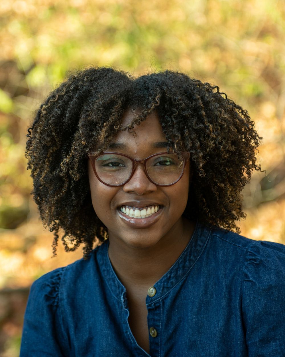 Cheerful portrait outdoors with natural curly hair and glasses against fall colors.