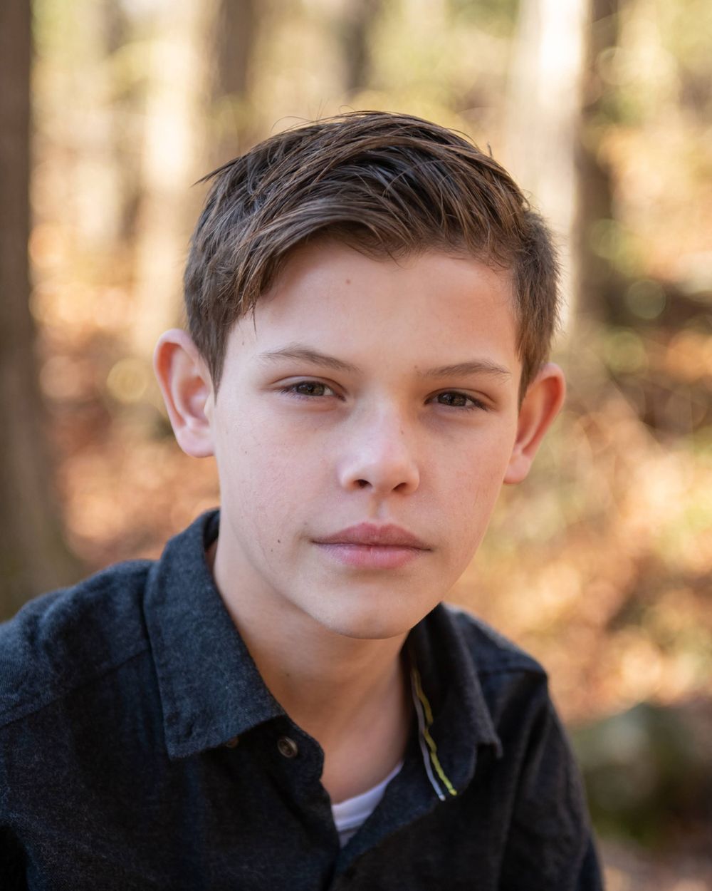 Portrait of young model in black collared shirt against blurred autumn background.